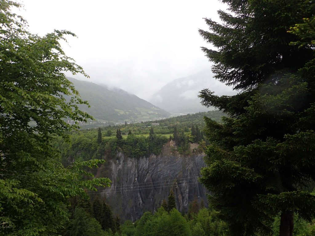 Mestia in the distance, the side of a chasm cut by a river in the foreground.